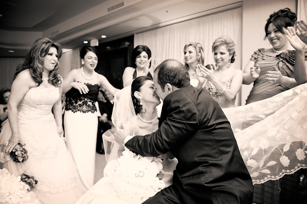 sepia photo - the happy bride and groom kissing at the ceremony while being surrounded by smiling happy bridesmaids - photo by Houston based wedding photographer Adam Nyholt